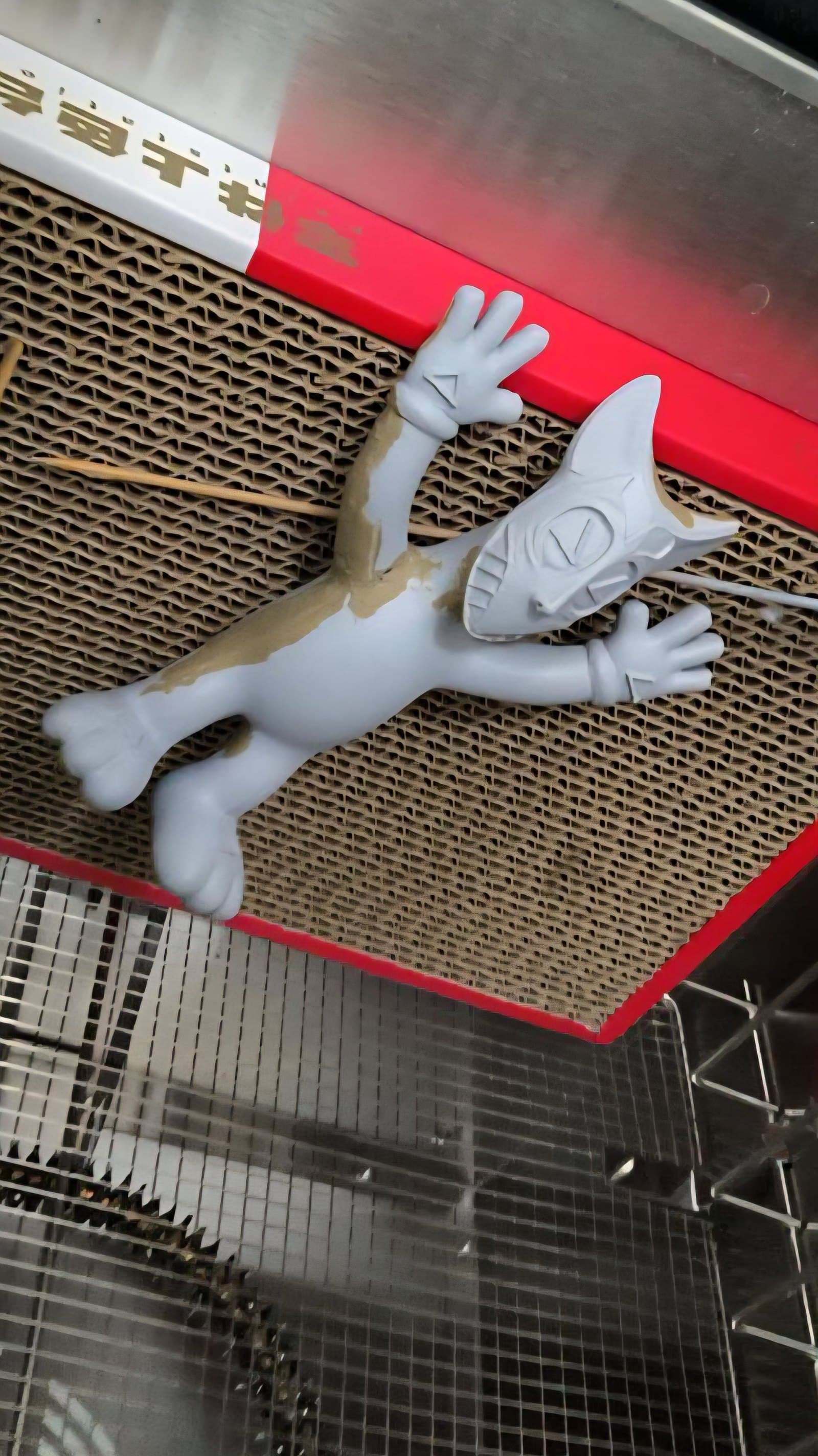 Raw 3D-printed Apophis figure in grey resin, mid-finishing — still showing print artifacts and a patch of unsanded surface. Sitting on cardboard on a workbench.