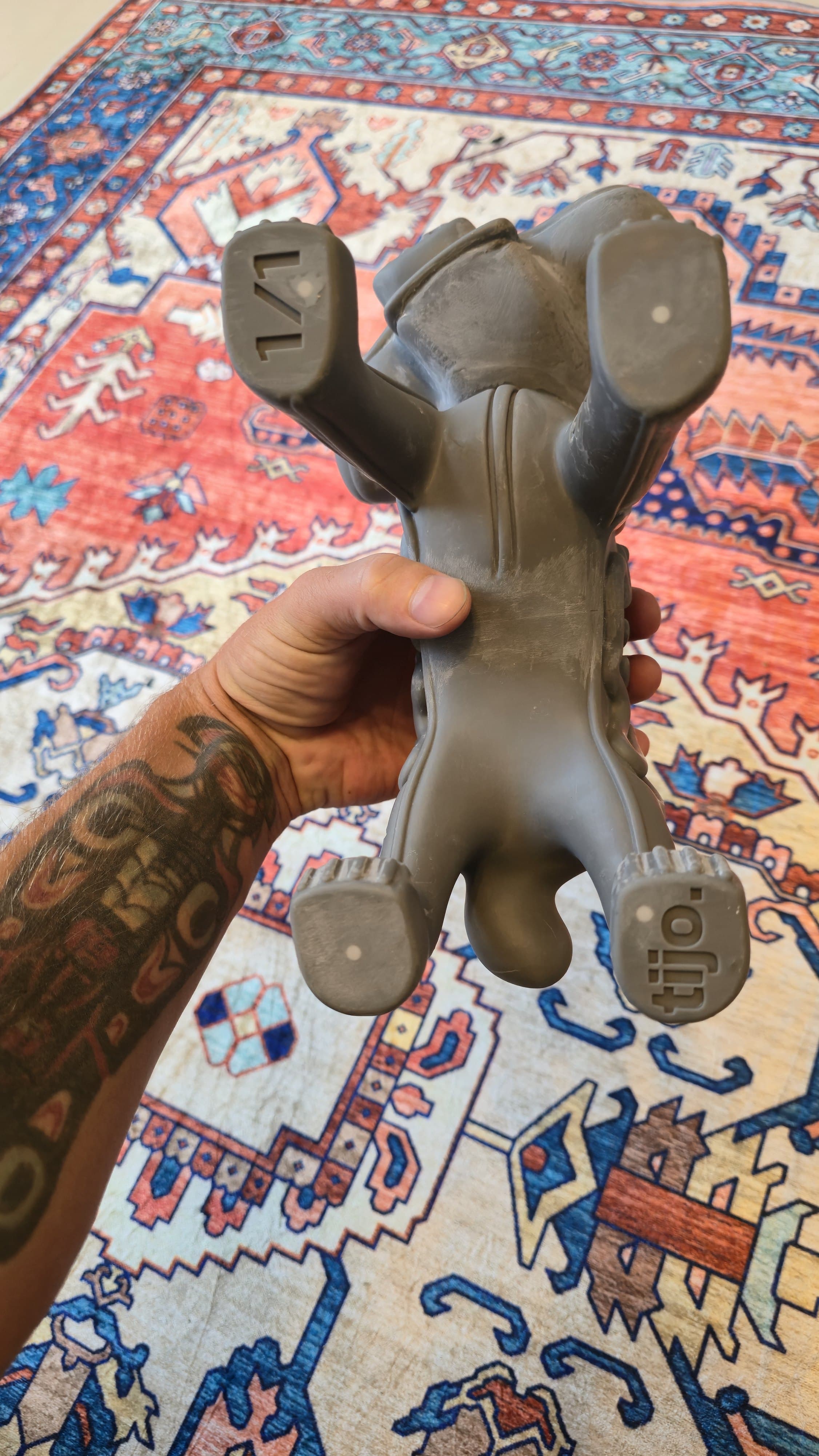 The raw gray Marley print held upside down in one hand over the carpet, showing the soles of its paws stamped 1/1 on one pad and tijo. on another.