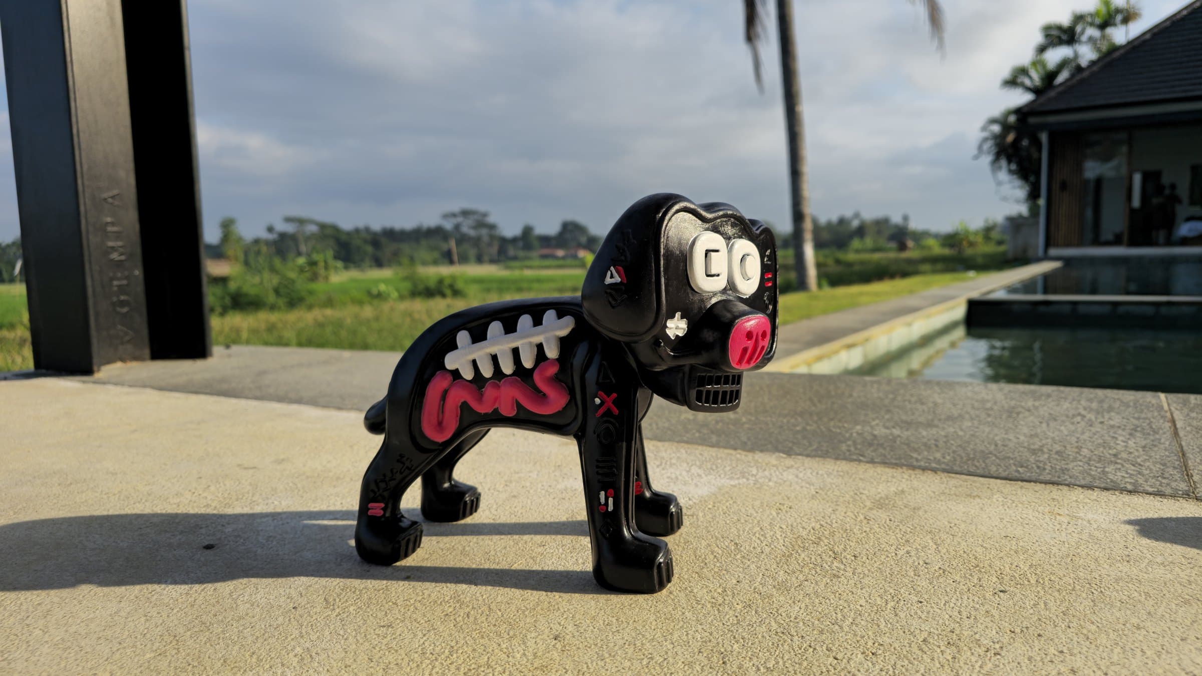 Finished Marley prototype in profile by the pool — the full white rib cage and pink intestinal coil down the black flank, glyphs picked out in white and red on the legs, palm trees and rice fields behind.