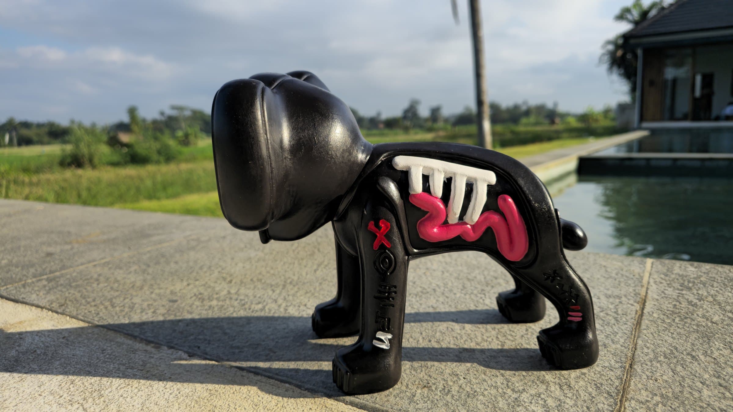 Finished Marley prototype from behind, head bowed — the glossy black head catching the sun, white ribs and pink coil visible along the far flank, standing at the edge of the pool.